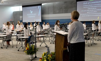 Nursing students in white coats and woman at podium